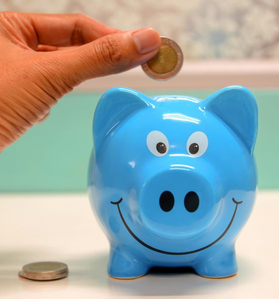 Hand inserting a coin into a blue piggy bank.